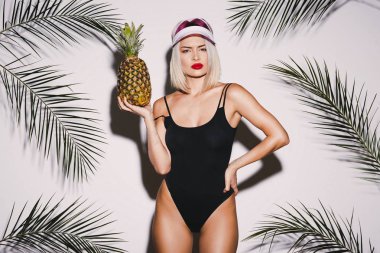Güzel kız yüzme takım elbise ve ananas ile pembe kap ayakta beyaz stüdyo arka plan üzerinde siyah sarı saçlı giyen ile