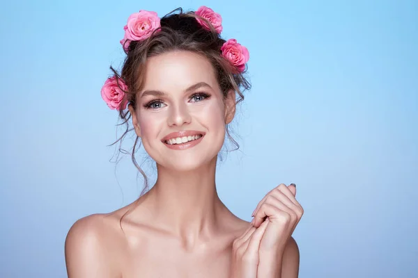 青い背景にポーズの髪にピンクのバラを持つ魅力的な若い女性の肖像画 — ストック写真