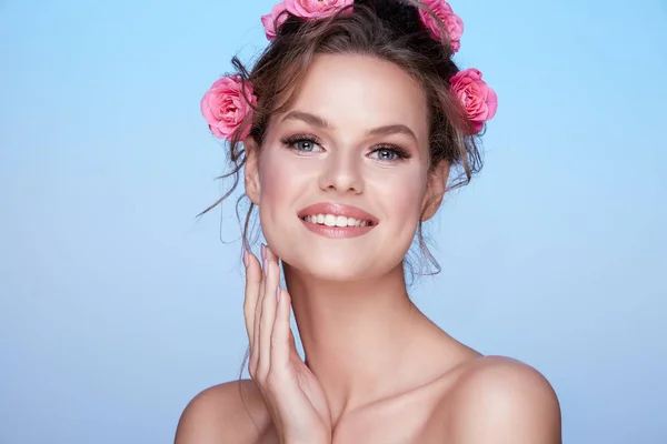 青い背景にポーズの髪にピンクのバラを持つ魅力的な若い女性の肖像画 — ストック写真