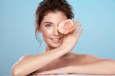 young attractive woman with bare shoulders and rose flower on blue background