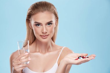 young blonde girl posing with pills and glass of water on blue c