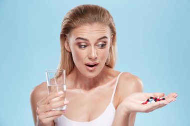 young blonde girl posing with pills and glass of water on blue c