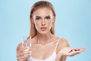 young blonde girl posing with pills and glass of water on blue c