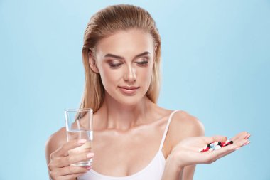 young blonde girl posing with pills and glass of water on blue c