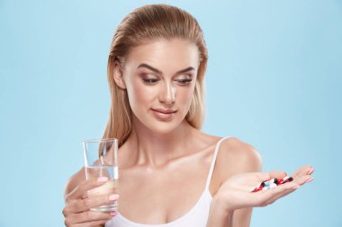 young blonde girl posing with pills and glass of water on blue c