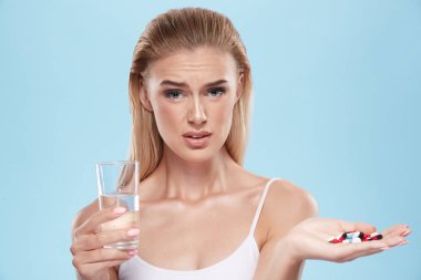 young blonde girl posing with pills and glass of water on blue c
