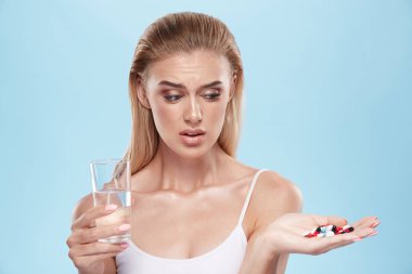young blonde girl posing with pills and glass of water on blue c