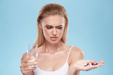 young blonde girl posing with pills and glass of water on blue c