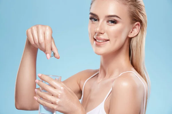 Mladá Blondýnka Dívka Ukazuje Pilulky Ruce Sklenice Vody Modré — Stock fotografie