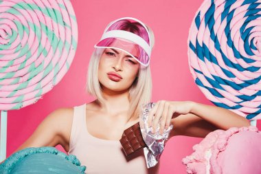 Pembe arka plan üzerinde çikolata ve büyük tatlılar ile ayakta sarı saçlı çekici kız