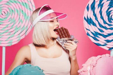 Pembe arka plan üzerinde çikolata ve büyük tatlılar ile ayakta sarı saçlı çekici kız