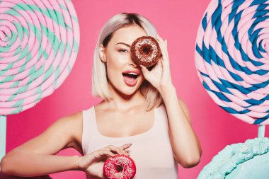 Pembe arka plan üzerinde çörek ve büyük tatlılar ile ayakta sarı saçlı çekici kız