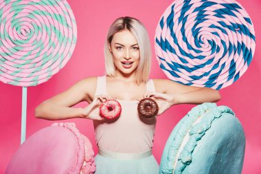 Pembe arka plan üzerinde çörek ve büyük tatlılar ile ayakta sarı saçlı çekici kız