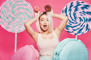 Pembe arka plan üzerinde çörek ve büyük tatlılar ile ayakta sarı saçlı çekici kız