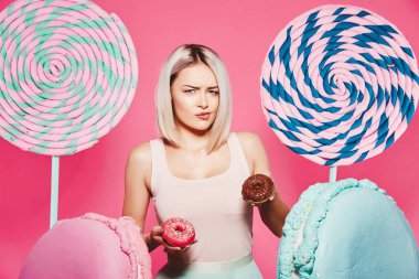 Pembe arka plan üzerinde çörek ve büyük tatlılar ile ayakta sarı saçlı çekici kız