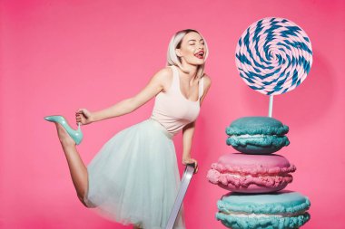 Pembe arka plan üzerinde büyük tatlılar ile ayakta sarı saçlı çekici kız