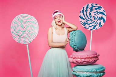 Pembe arka plan üzerinde büyük tatlılar ile ayakta sarı saçlı çekici kız