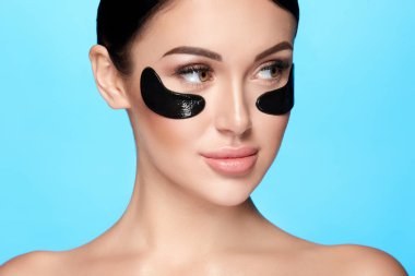 mavi arka plan üzerinde yüzünde çıplak makyaj ve göz yamaları ile genç kadın portresi