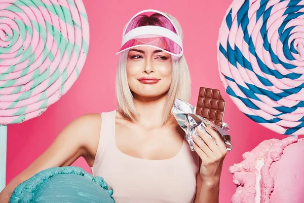 Pembe arka plan üzerinde çikolata ve büyük tatlılar ile ayakta sarı saçlı çekici kız