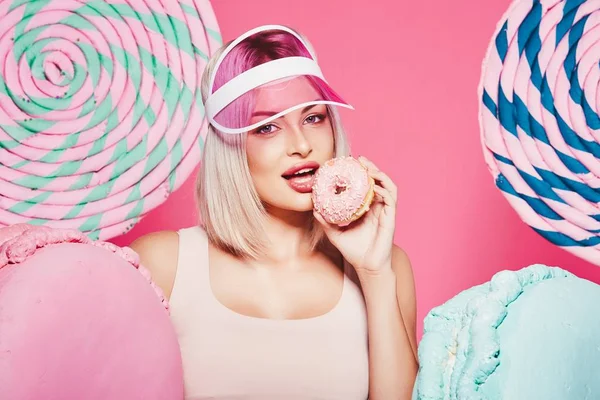Pembe arka plan üzerinde çörek ve büyük tatlılar ile ayakta sarı saçlı çekici kız