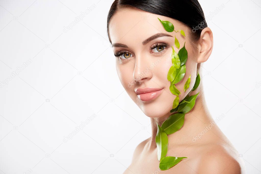 portrait of young woman with nude makeup and green leaves on face on white background