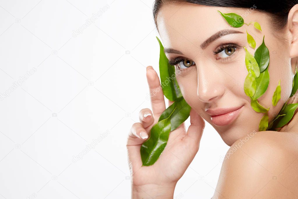 portrait of young woman with nude makeup and green leaves on face on white background