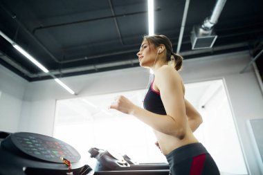 Spor salonunda koşu bandında egzersiz yapan genç ve formda bir kadın.