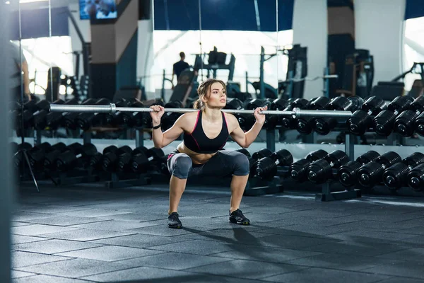 athletic sportswoman squatting in gym alone