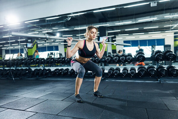 athletic sportswoman squatting in gym alone