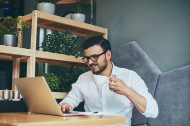 young handsome businessman in eyeglasses with cup of coffee working in cafe