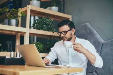 young handsome businessman in eyeglasses with cup of coffee working in cafe