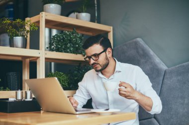 young handsome businessman in eyeglasses with cup of coffee working in cafe