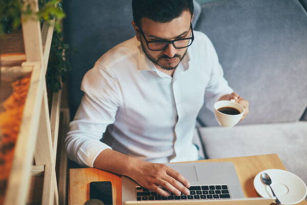 young handsome businessman in eyeglasses with cup of coffee working in cafe