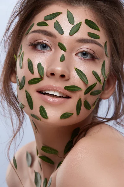 灰色の背景に顔に緑の葉を持つ魅力的な女性 — ストック写真