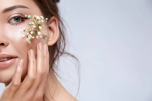 beautiful tender woman with flowers on face posing on grey backdrop