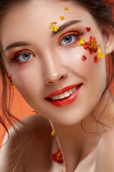 オレンジ色の背景に顔に花を持つ魅力的な女性の肖像画 — ストック写真
