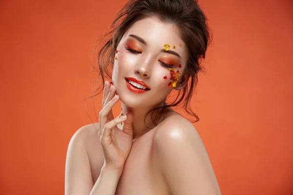 オレンジ色の背景に顔に花を持つ魅力的な女性の肖像画 — ストック写真