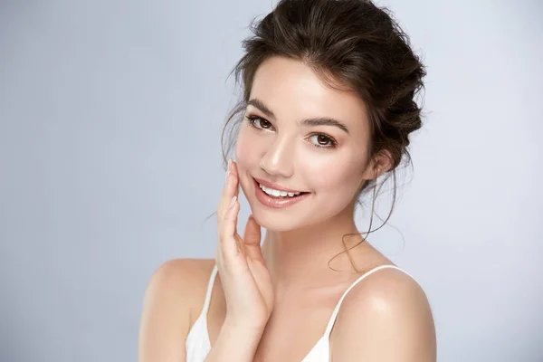 Parlak gülüşü ve yanağına dokunan küçük bukleleri olan ve kameraya bakan güzel bir kız.