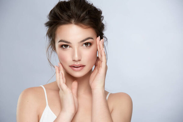 attractive female with tiny curls and natural make-up touching face and looking to camera