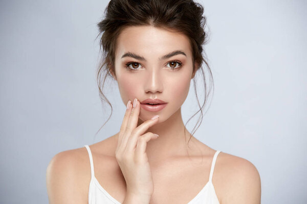 sexy model with perfect skin and dark eyes looking to camera and touching face with arm