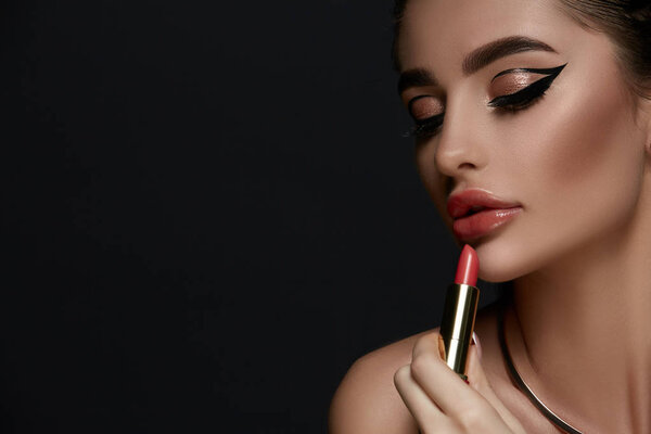 glamorous woman with evening make-up holding red lipstick and looking down, luxury evening makeup 