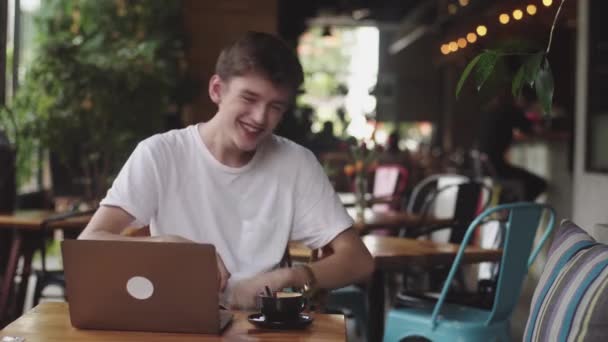 年轻的欧洲男子微笑和笑在咖啡馆，自由职业者和博客有有趣的聊天室内，现代沟通在线连接在咖啡馆。在餐厅打开笔记本电脑. — 图库视频影像