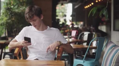 Genç Adam cep telefonu, kullanışlı dokunmatik ve kafede metin mesajı gönderme internette sörf. Yakışıklı Genç halka açık bir yerde mobil uygulamada sohbet. 
