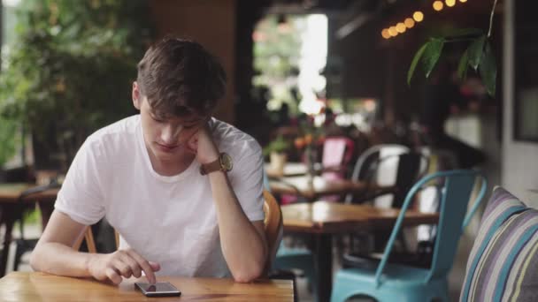 Jonge man surfen op internet in mobiele telefoon, handige aanraking en het verzenden van tekstbericht in café. Knappe tiener chatten in mobiele app in openbare plaats. — Stockvideo