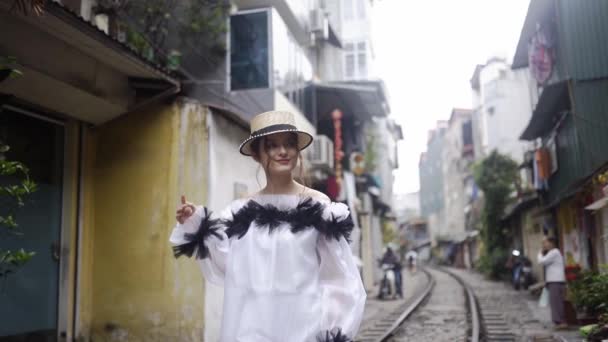 古い建物の間に鉄道でアジアの通りを歩く美しく、若いファッションのメスティーゾの女の子。ベトナムの観光地での旅のコンセプト。白いファッショナブルなドレスでかわいい女性. — ストック動画