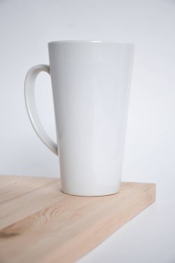 Beyaz arka plan üzerinde ahşap masa kenarına yüksek beyaz kupa