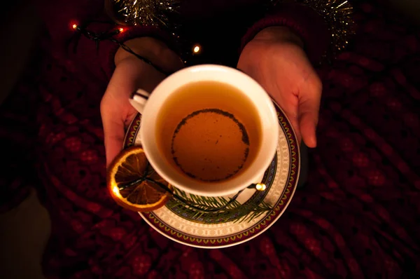 Kadın elleriyle çay ve garland. Yeni yıl siyah çay elinde. Ladin ve turuncu siyah çay.