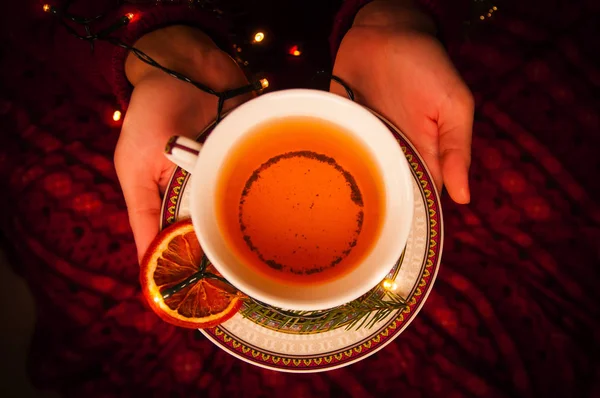 Kadın elleriyle çay ve garland. Yeni yıl siyah çay elinde. Ladin ve turuncu siyah çay.