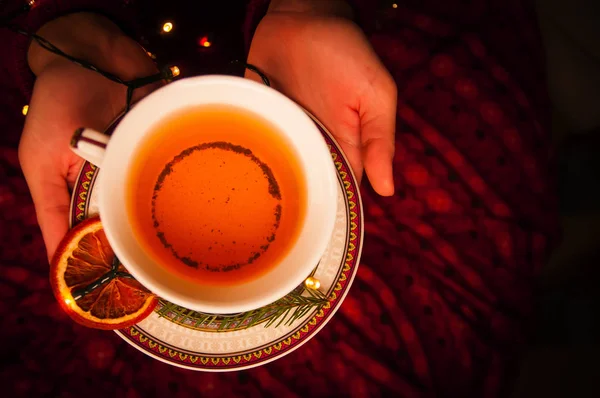 Kadın elleriyle çay ve garland. Yeni yıl siyah çay elinde. Ladin ve turuncu siyah çay.