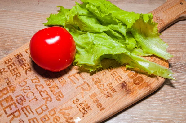 Yeşil salata ve mutfak masası ve ahşap arka plan üzerinde kırmızı domates.